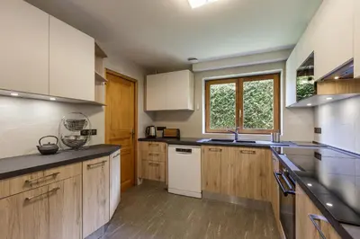 a large kitchen with wooden cabinets and white appliances at Arve - Chalet 4CH Jardin Nature Vues BBQ Poele in Chamonix-Mont-Blanc
