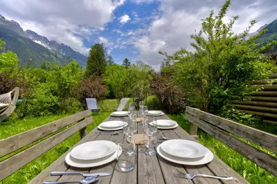 a wooden table with plates and wine glasses on it at Mouilles - Apart 113m2 Jardin Calme Garage Bar Centre in Chamonix-Mont-Blanc