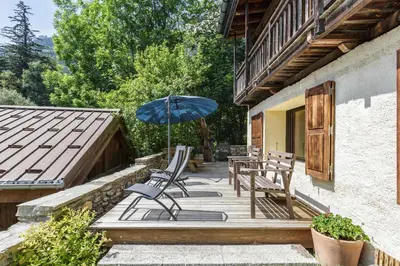 a patio with a table and chairs and an umbrella at Lavancher - Chalet 400m2 Ferme 1803 renovee Sauna Billard in Chamonix-Mont-Blanc