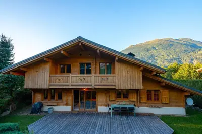 a large wooden house with a deck and mountains at Glaciers Chalet Cheminee Vue Confort Calme in Les Houches
