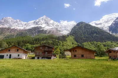 a group of houses in a field with mountains in the background at Couchant Chalet Lumineux 6pax Vues Terrasses Confort in Chamonix-Mont-Blanc