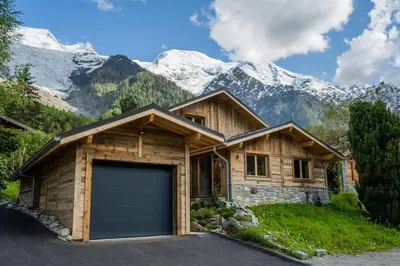 a wooden house with a garage in front of mountains at Eden Chalet Spacieux Vues Jacuzzi Cheminee BBQ in Chamonix-Mont-Blanc