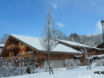 a log cabin in the snow with a tree at Appartement neuf 3 pièces - 6 pers - Vue montagne - FR-1-815-49 in Samoëns