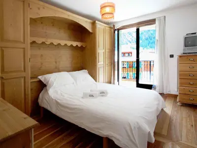 a bedroom with a large white bed with a wooden headboard at Apartment Charmante Wohnung in Chamonix mit Südbalkon und Blick auf den Blanc by Interhome in Chamonix-Mont-Blanc