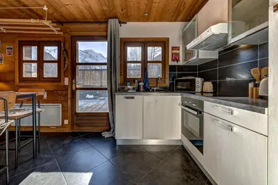 a kitchen with white cabinets and a table and some windows at Tiny Chalet - near to Servoz train station in Les Houches
