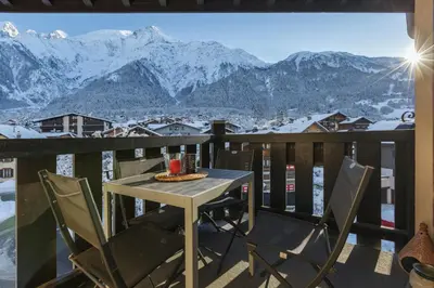 a table and chairs on a balcony with snow covered mountains at La Verte Appart 2CH familial 5mn pistes Vue Parking in Les Houches
