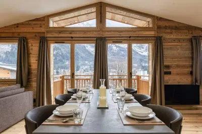 a dining room with a table and chairs and windows at Ocma3 Somptueux 6pax VueMtBlanc Central Parking in Chamonix-Mont-Blanc