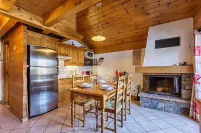 a kitchen with a table and a refrigerator and a fireplace at Verny Appart 2CH Familiale Pied Pistes Piscine Vue in Les Houches