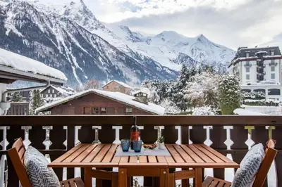 a wooden table on a balcony with snow covered mountains at Savoy Cosy 1CH pied pistes Hypercentre Vue MtBlanc in Chamonix-Mont-Blanc