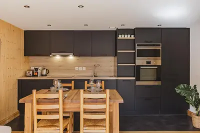 a kitchen with black cabinets and a wooden table at Savoy Cosy 1CH pied pistes Hypercentre Vue MtBlanc in Chamonix-Mont-Blanc