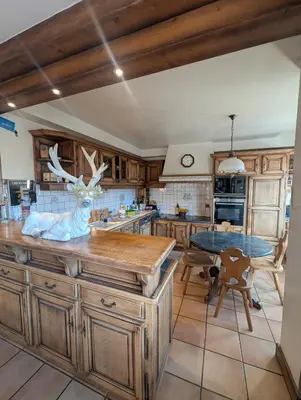 a kitchen with wooden cabinets and a counter with a table at Chez Math et Lolo in Sallanches