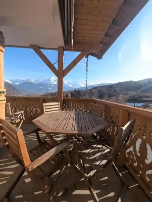 a wooden table and chairs on a balcony with mountains at Chez Math et Lolo in Sallanches
