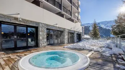 a hot tub on a deck in front of a building at Pied des pistes, piscine, jacuzzi in Flaine