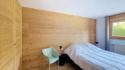 a bedroom with a wooden wall with a bed and a chair at 1 Riante Colline Arnica - PROCHE CENTRE in Megève