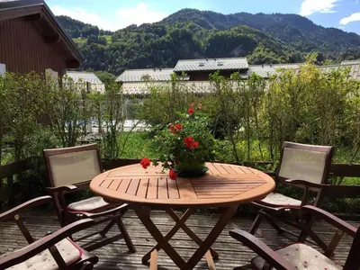 a wooden table with a vase of flowers on a patio at Charmant 3 Pièces Sud, Piscine & Animaux Acceptés - FR-1-629-155 in Samoëns