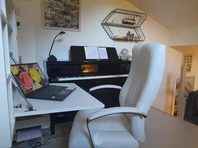 a desk with a laptop and a chair next to a piano at Chalet mitoyen au calme - rez-de-jardin - parking in Les Houches