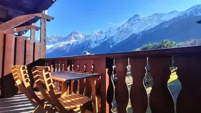 a wooden table and chairs on a balcony with mountains at Beau studio dans un chalet in Les Houches