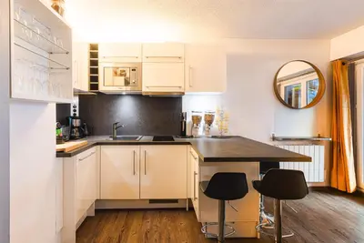 a kitchen with white cabinets and a sink and two stools at Vue montagne parking privé balcon in Chamonix-Mont-Blanc