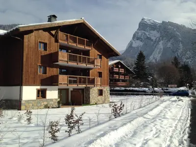 a wooden building in the snow with a mountain at Résidence Les Chardons Argentés in Samoëns