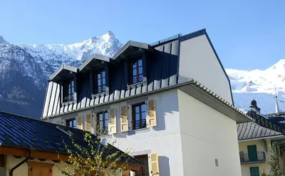 a white building with mountains in the background at Hotel Du Clocher in Chamonix-Mont-Blanc
