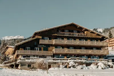 a large wooden building with snow in front of it at Hôtel Les Roches Fleuries in Cordon