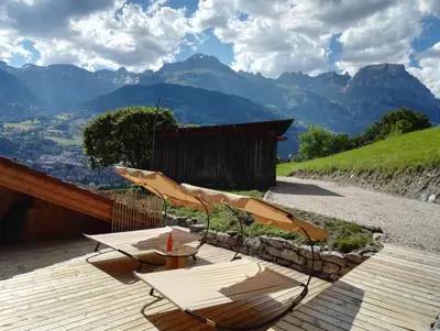 a group of tables and chairs on a deck with mountains at Chantemerle 1741, chambres d'hôtes à la montagne in Sallanches