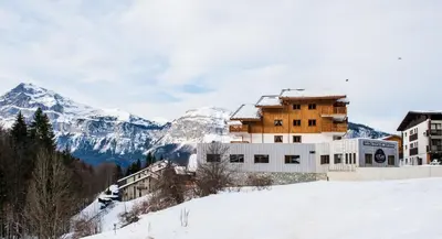 a building in the snow with mountains in the background at CGH Résidence Boutique Les Chalets de Léana in Les Carroz d'Araches