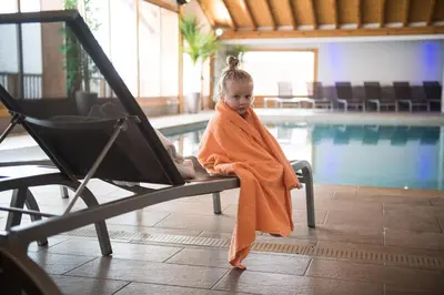 a little girl wrapped in a towel sitting next to a swimming pool at CGH Résidence Boutique Les Chalets de Léana in Les Carroz d'Araches