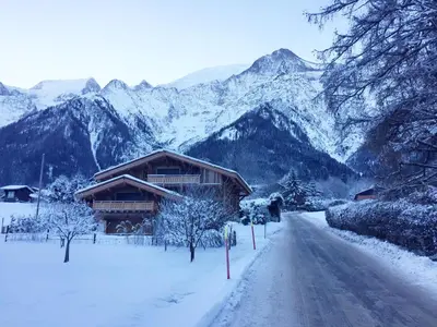 a snow covered road next to a lodge with mountains at Chalet Alexandra in Les Houches