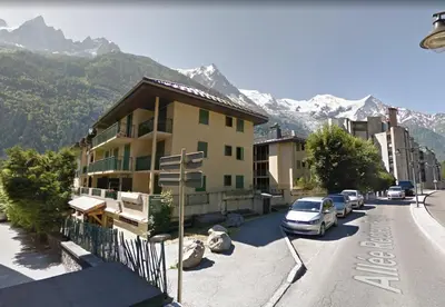 a building with cars parked in a parking lot with mountains at La Chabane in Chamonix-Mont-Blanc