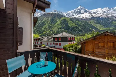 a table with a bottle of wine on a balcony with mountains at APARTMENT CHAMOUNY - Alpes Travel - Chamonix - Sleeps 8 in Chamonix-Mont-Blanc