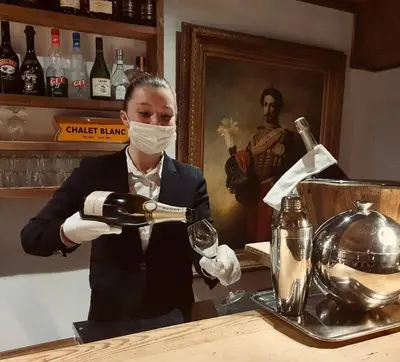 a woman in a mask pouring a glass of wine at Le Chalet Blanc in Megève