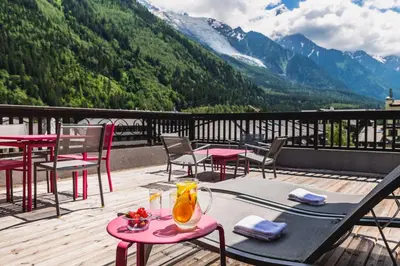 a patio with tables and chairs on a balcony with mountains at Hotel Le Morgane in Chamonix-Mont-Blanc