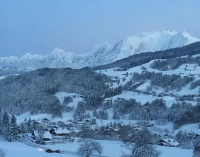 a village in the snow with mountains in the background at Ferme Vauvray in Megève