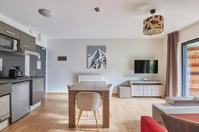 a kitchen and living room with a wooden table in a room at Résidence Odalys Isatis in Chamonix-Mont-Blanc
