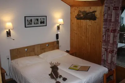 a teddy bear sitting on a bed with a book at Logis Hotel Gai Soleil in Samoëns