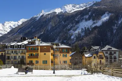 a person sitting on a bench in the snow in front of buildings at Hôtel Lyret in Chamonix-Mont-Blanc