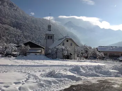 a church covered in snow in front of a mountain at Résidence Les Jorasses in Servoz