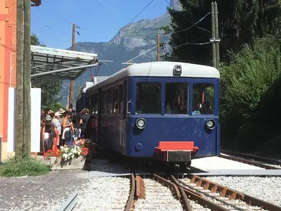 a blue train pulling into a train station with people at Les Jardins Alpins - Apartment in Saint-Gervais-les-Bains