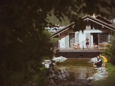two people standing in the water in front of a house at Le Hameau Albert 1er - Relais & Châteaux in Chamonix-Mont-Blanc
