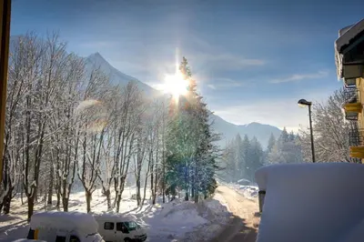 a snow covered street with the sun shining on a tree at Vert Lodge Chamonix in Chamonix-Mont-Blanc