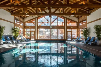 a pool in a house with chairs and windows at CGH Résidences & Spas La Reine des Prés in Samoëns