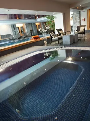 a large swimming pool in a hotel lobby with chairs at CGH Résidences & Spas Les Chalets de Jouvence in Les Carroz d'Araches