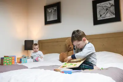 two young boys sitting on a bed reading a book at CGH Résidences & Spas Les Chalets de Jouvence in Les Carroz d'Araches