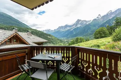 a table and chairs on a balcony with mountains at APARTMENT REFUGE DE BELLACHAT - Alpes Travel - Les Houches - Sleeps 4 in Les Houches