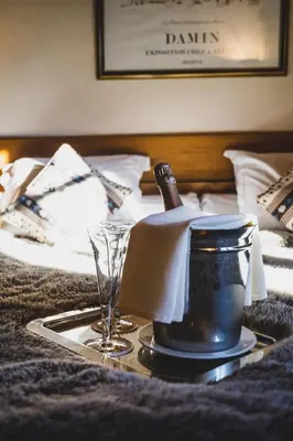a tray with a bottle of wine and glasses on a bed at Hôtel La Grange d'Arly in Megève