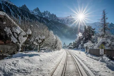 a snow covered train tracks with the sun in the background at Eden Hotel, Apartments and Chalet Chamonix Les Praz in Chamonix-Mont-Blanc