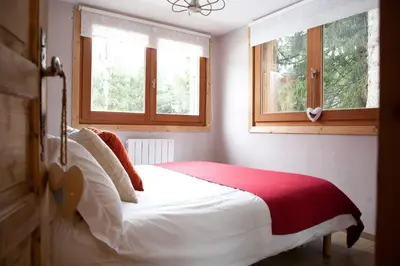 a bedroom with a bed with a red blanket and two windows at Chalet Les Favrands in Chamonix-Mont-Blanc