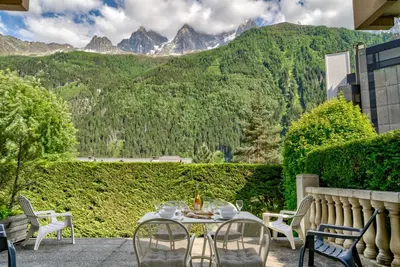 a patio with a table and chairs with mountains in the background at Villa Floria Apartment in Chamonix-Mont-Blanc