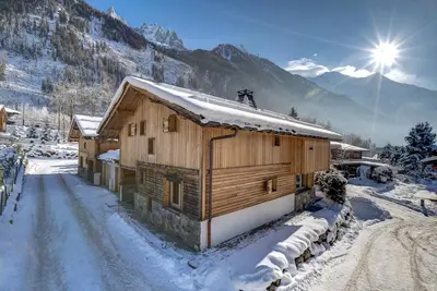a wooden cabin in the snow with the sun behind it at Chalet Planards 1 in Chamonix-Mont-Blanc